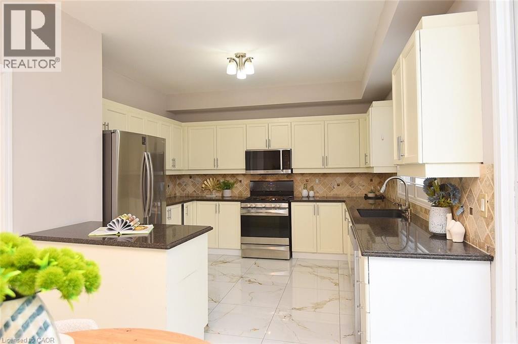 Kitchen featuring stainless steel appliances, light marble finish flooring, dark stone counters, and tasteful backsplash - 5109 Blue Spruce Avenue, Burlington, ON - Indoor Photo Showing Kitchen