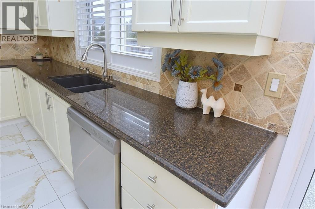 Kitchen featuring tasteful backsplash, dishwasher, white cabinetry, light marble finish floors, and dark stone countertops - 5109 Blue Spruce Avenue, Burlington, ON - Indoor Photo Showing Kitchen With Double Sink