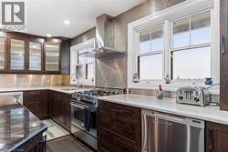 Kitchen with backsplash, a healthy amount of sunlight, wall chimney range hood, and appliances with stainless steel finishes -
