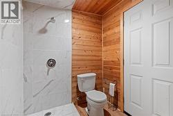 Bathroom with wood walls, wooden ceiling, toilet, a tile shower, and wood-type flooring -