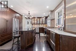 Kitchen with stainless steel appliances, wall chimney range hood, decorative light fixtures, an inviting chandelier, and a center island -