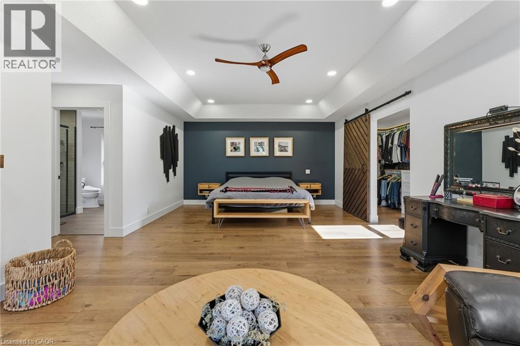 Bedroom with a barn door, a spacious closet, light wood-style flooring, ceiling fan, and a tray ceiling - 115 Lakeshore Road, Port Burwell, ON - Indoor