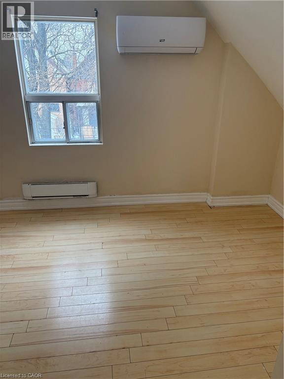 Additional living space with a wall mounted air conditioner, light wood finished floors, a baseboard radiator, and lofted ceiling - 95 Sanford Avenue N, Hamilton, ON - Indoor Photo Showing Other Room