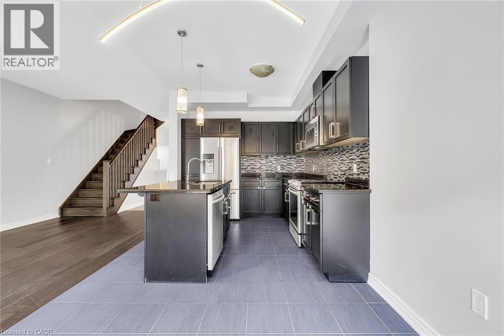 Kitchen with stainless steel appliances, decorative light fixtures, an island with sink, tasteful backsplash, and dark stone counters - 89 Sonoma Valley Crescent, Hamilton, ON - Indoor Photo Showing Kitchen With Stainless Steel Kitchen With Upgraded Kitchen