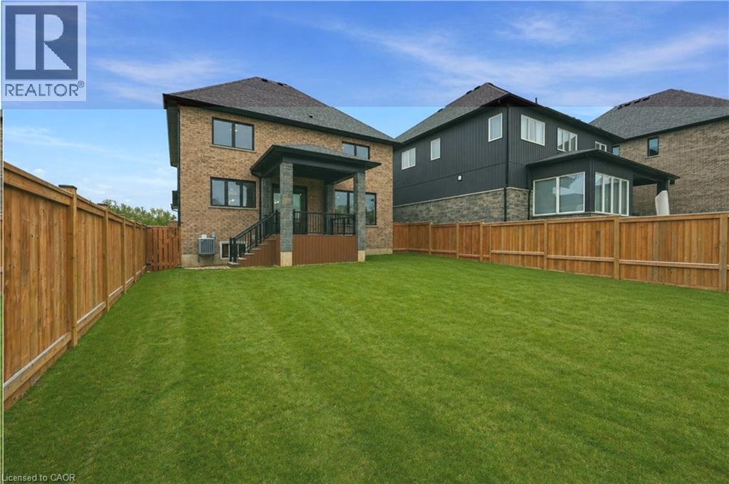 Expansive lawn featuring a covered porch with stone columns and black railings, light brown privacy fencing, and a brick and siding exterior - 7 Bartlett Avenue, Grimsby, ON - Outdoor