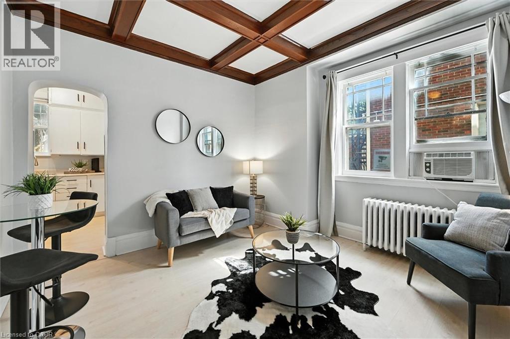 Living room with coffered ceiling, radiator, beamed ceiling, light wood-style flooring, and arched walkways - 1047 Main Street E, Hamilton, ON - Indoor Photo Showing Living Room