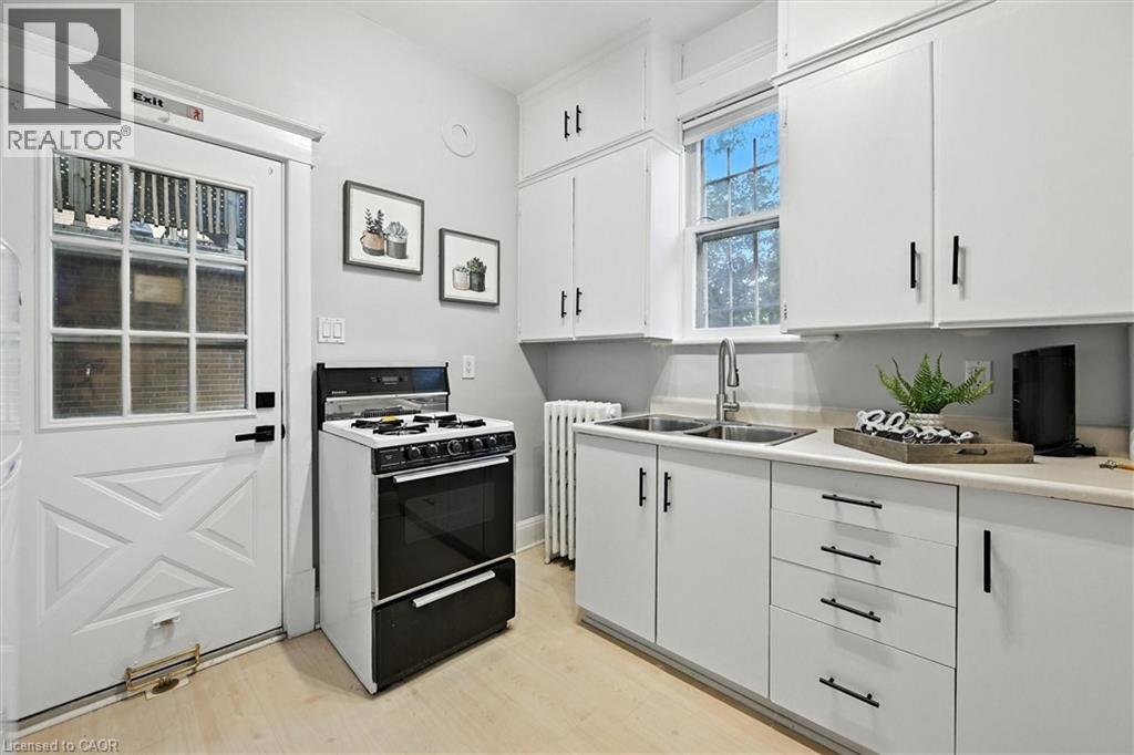 Kitchen featuring light countertops, white cabinetry, gas range oven, radiator, and light wood-style flooring - 1047 Main Street E, Hamilton, ON - Indoor Photo Showing Kitchen With Double Sink