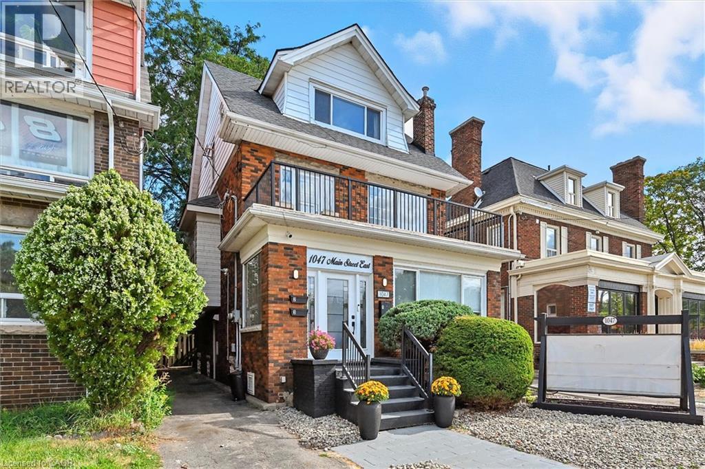 View of front facade featuring brick siding, a balcony, and a shingled roof - 1047 Main Street E, Hamilton, ON - Outdoor With Facade