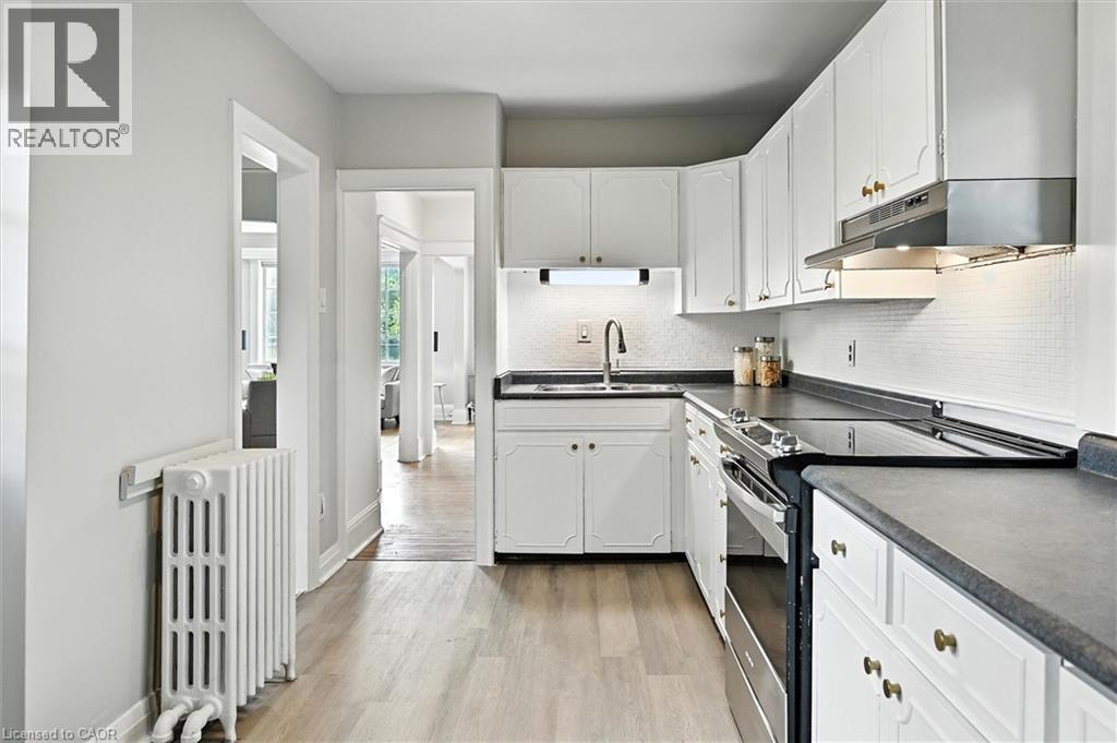 Kitchen with stainless steel electric stove, dark countertops, radiator heating unit, and under cabinet range hood - 1047 Main Street E, Hamilton, ON - Indoor Photo Showing Kitchen With Double Sink