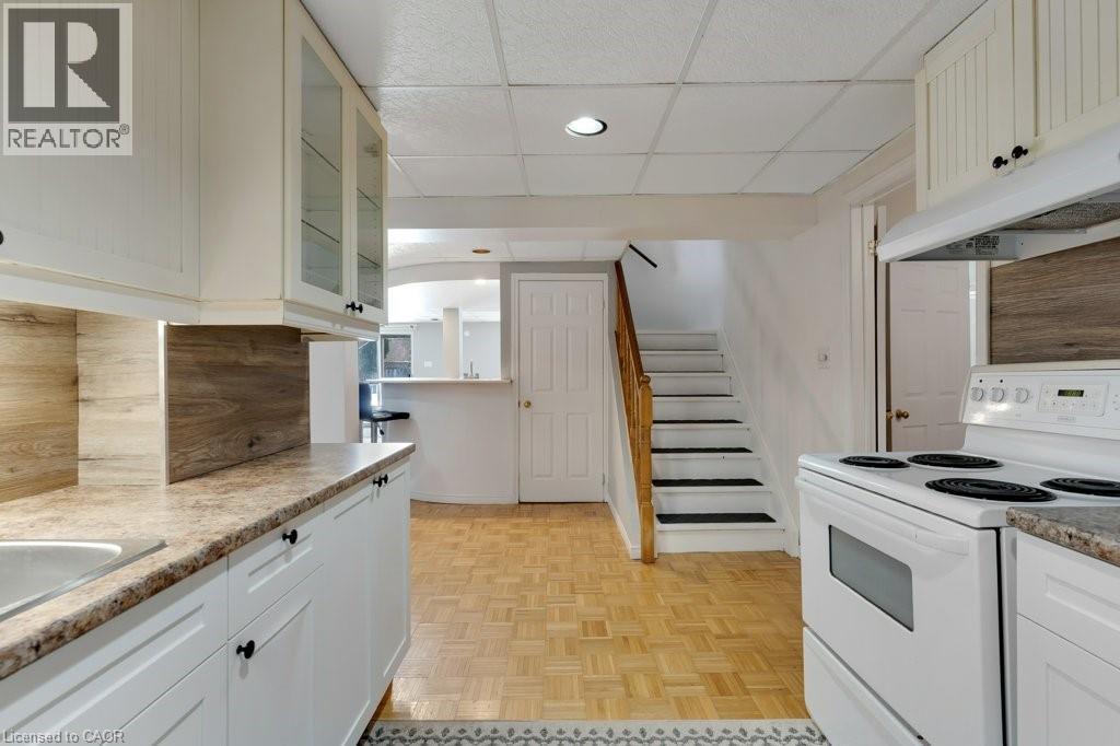 Lower Kitchen with white range with electric cooktop, glass fronted cabinets, a paneled ceiling, white cabinetry, and light countertops - 148 Cowan Boulevard, Cambridge, ON - Indoor Photo Showing Kitchen