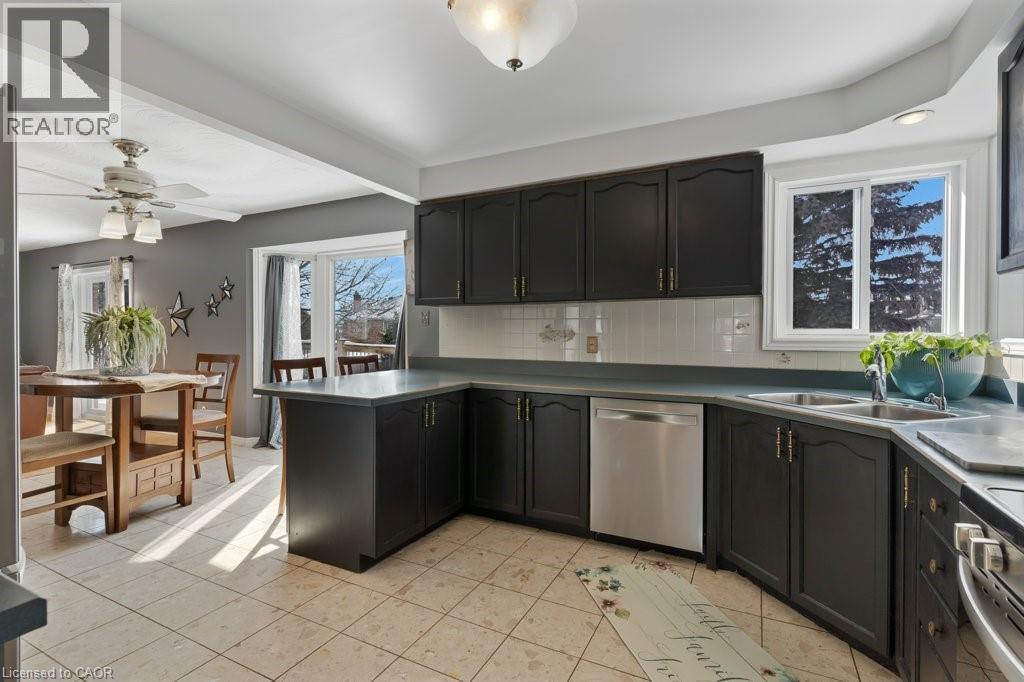 Kitchen featuring ceiling fan, stainless steel appliances, backsplash, dark countertops, and light tile patterned flooring - 148 Cowan Boulevard, Cambridge, ON - Indoor Photo Showing Kitchen With Double Sink