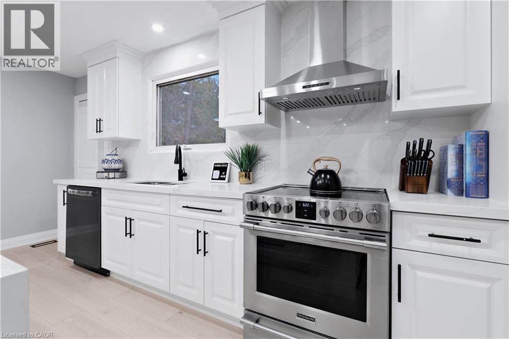 Kitchen featuring stainless steel electric stove, wall chimney exhaust hood, light stone counters, dishwasher, and white cabinetry - 19 Broad Street, Brantford, ON - Indoor Photo Showing Kitchen With Upgraded Kitchen