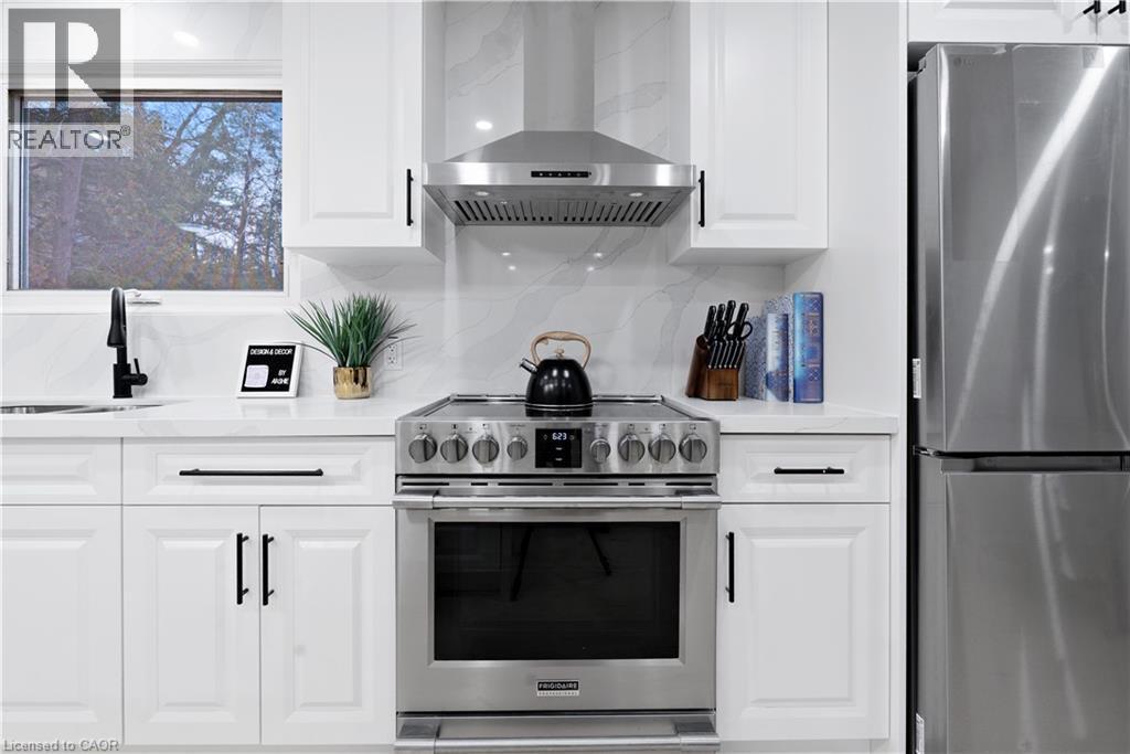 Kitchen featuring appliances with stainless steel finishes, wall chimney exhaust hood, white cabinetry, light stone countertops, and backsplash - 19 Broad Street, Brantford, ON - Indoor Photo Showing Kitchen With Stainless Steel Kitchen With Upgraded Kitchen
