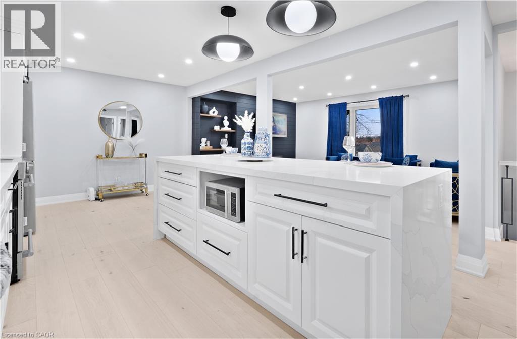 Kitchen with white cabinets, light stone counters, recessed lighting, an island with sink, and stainless steel microwave - 19 Broad Street, Brantford, ON - Indoor