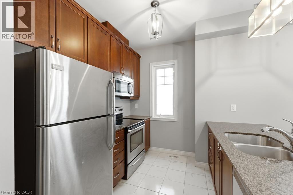 Kitchen featuring dark stone counters, stainless steel appliances, wood finish cabinetry, and light tile patterned flooring - 4 Andruss Lane, Ancaster, ON - Indoor Photo Showing Kitchen With Stainless Steel Kitchen With Double Sink