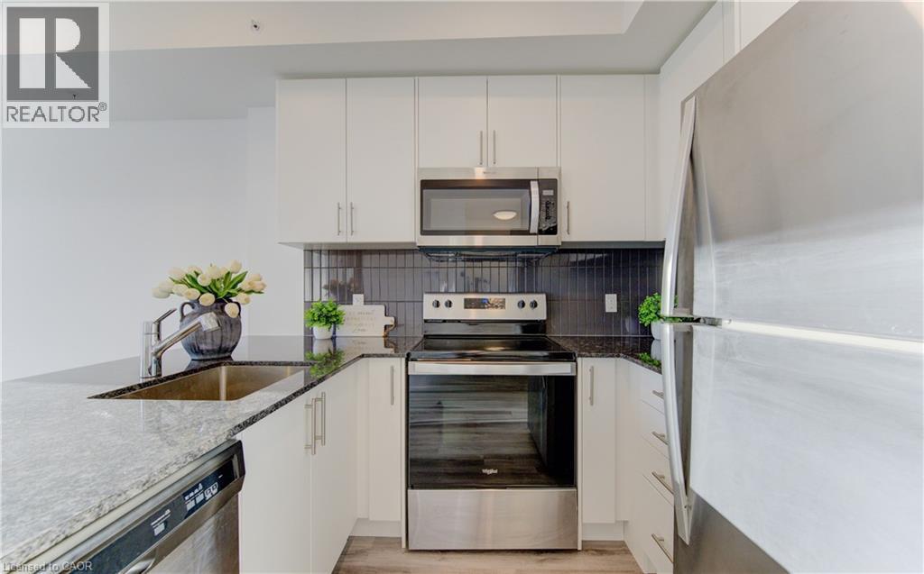 Kitchen featuring stainless steel appliances, dark stone counters, white cabinetry, and light wood-style floors - 103 Roger Street Unit# 310, Waterloo, ON - Indoor Photo Showing Kitchen With Stainless Steel Kitchen