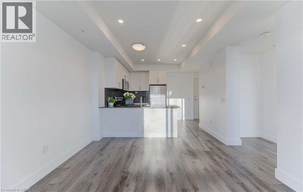 Kitchen featuring a tray ceiling, open floor plan, white cabinets, a peninsula, and backsplash - 103 Roger Street Unit# 310, Waterloo, ON - Indoor Photo Showing Kitchen