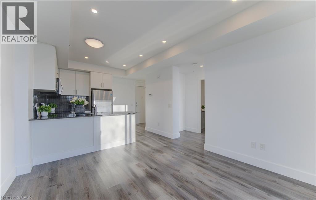 Kitchen with white cabinets, stainless steel appliances, light wood-type flooring, dark stone counters, and open floor plan - 103 Roger Street Unit# 310, Waterloo, ON - Indoor Photo Showing Kitchen