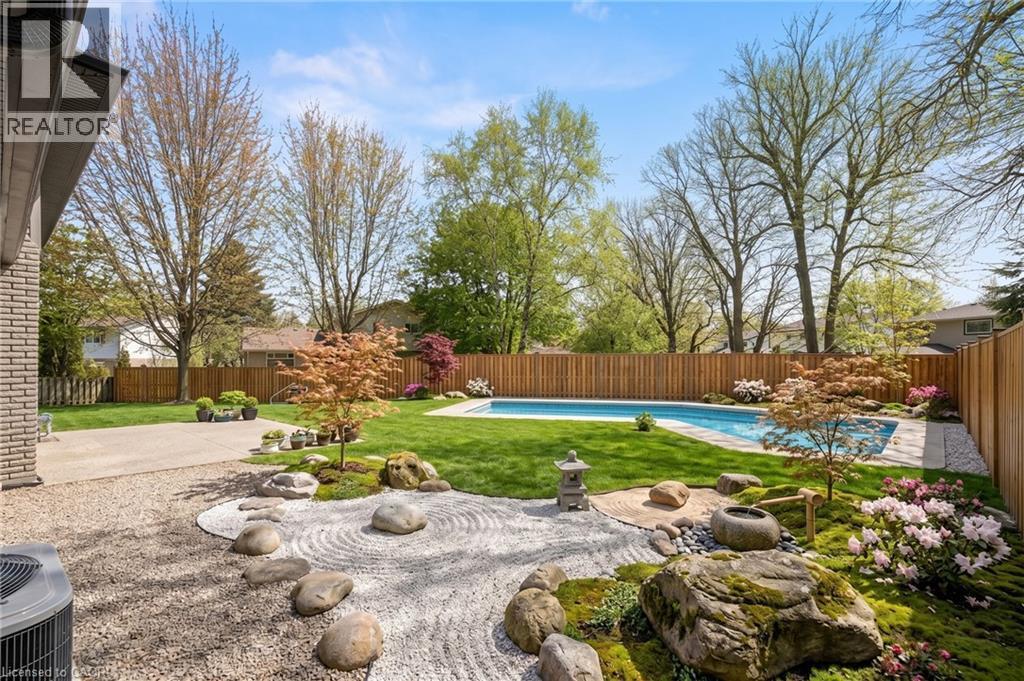 Expansive backyard featuring a central swimming pool, lush green lawn, and a curated rock garden with raked gravel - 361 Coleridge Place, Waterloo, ON - Outdoor With In Ground Pool With Backyard