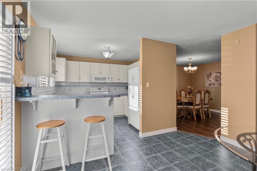Kitchen with a kitchen bar, dark tile patterned flooring, a peninsula, white appliances, and tasteful backsplash - 42 Archer Way, Hamilton, ON - Indoor Photo Showing Kitchen