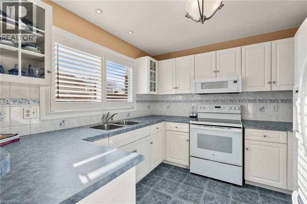 Kitchen featuring glass fronted cabinets, white appliances, dark countertops, and white cabinets - 42 Archer Way, Hamilton, ON - Indoor Photo Showing Kitchen With Double Sink