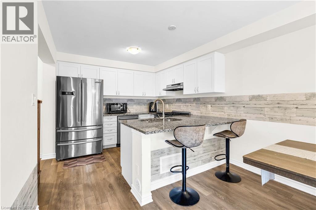 Kitchen with dark stone countertops, white cabinetry, appliances with stainless steel finishes, a breakfast bar area, and dark wood-type flooring - 143 Ridge Road Unit# 48, Cambridge, ON - Indoor Photo Showing Kitchen