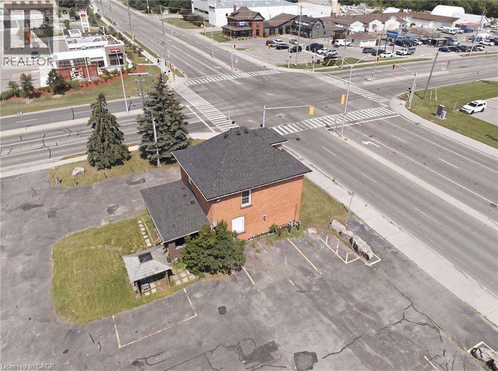 Brick structure with a dark shingle roof, featuring an asphalt parking lot and adjacent green space - 1360 Rymal Road E, Hamilton, ON