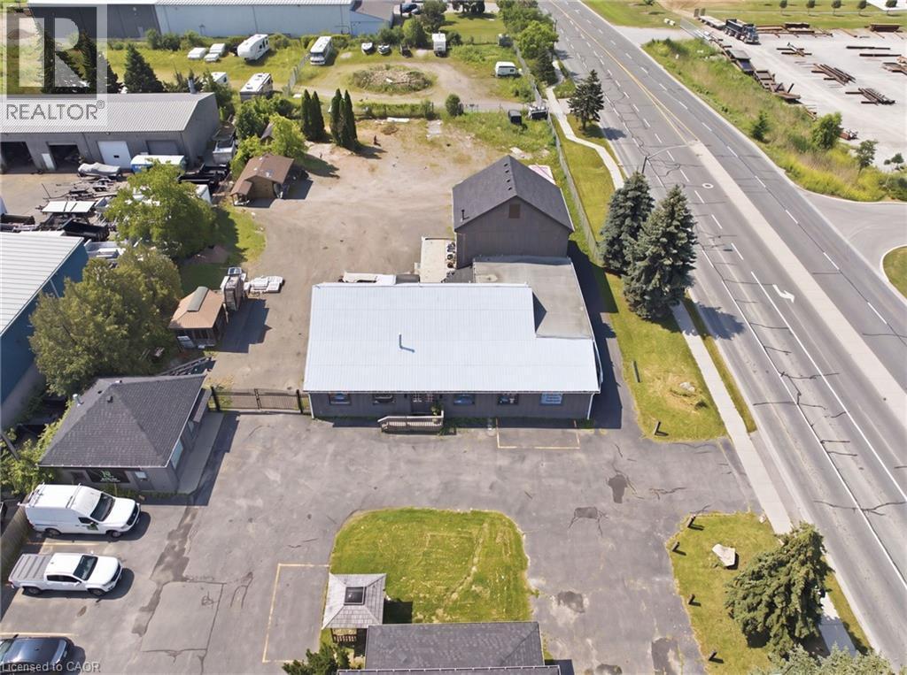 Commercial property featuring a main building with a metal roof, a smaller auxiliary building with a shingled roof, extensive paved parking, a gravel lot, and direct frontage onto a multi-lane roadway - 1360 Rymal Road E, Hamilton, ON