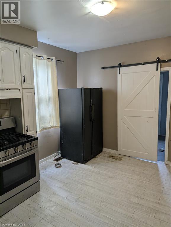 Kitchen featuring stainless steel range with gas cooktop, a barn door, black refrigerator with ice dispenser, light wood-type flooring, and white cabinetry - 151 Gibson Avenue, Hamilton, ON - Indoor Photo Showing Kitchen