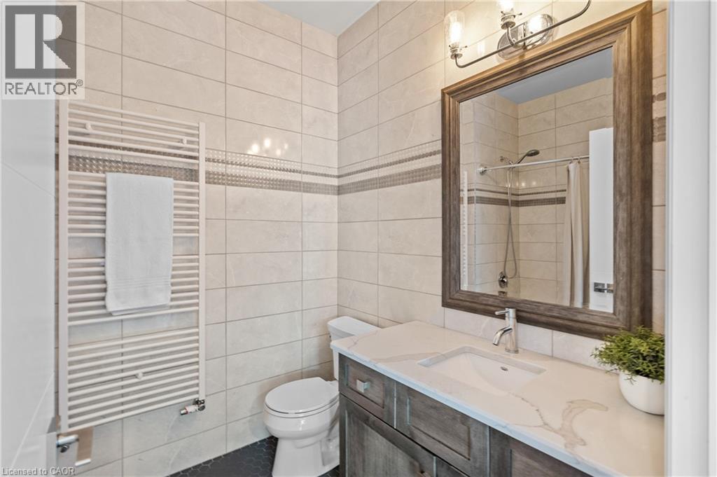 Full bath featuring a towel warmer, radiator heating unit, vanity, tile walls, and a tile shower - 25 Concession Street Unit# 201, Cambridge, ON - Indoor Photo Showing Bathroom