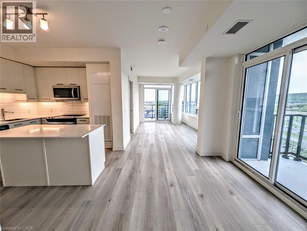 Kitchen featuring light wood-style floors, stainless steel microwave, tasteful backsplash, a kitchen island, and light stone counters - 385 Winston Road Unit# 1311, Grimsby, ON - Indoor Photo Showing Kitchen With Upgraded Kitchen
