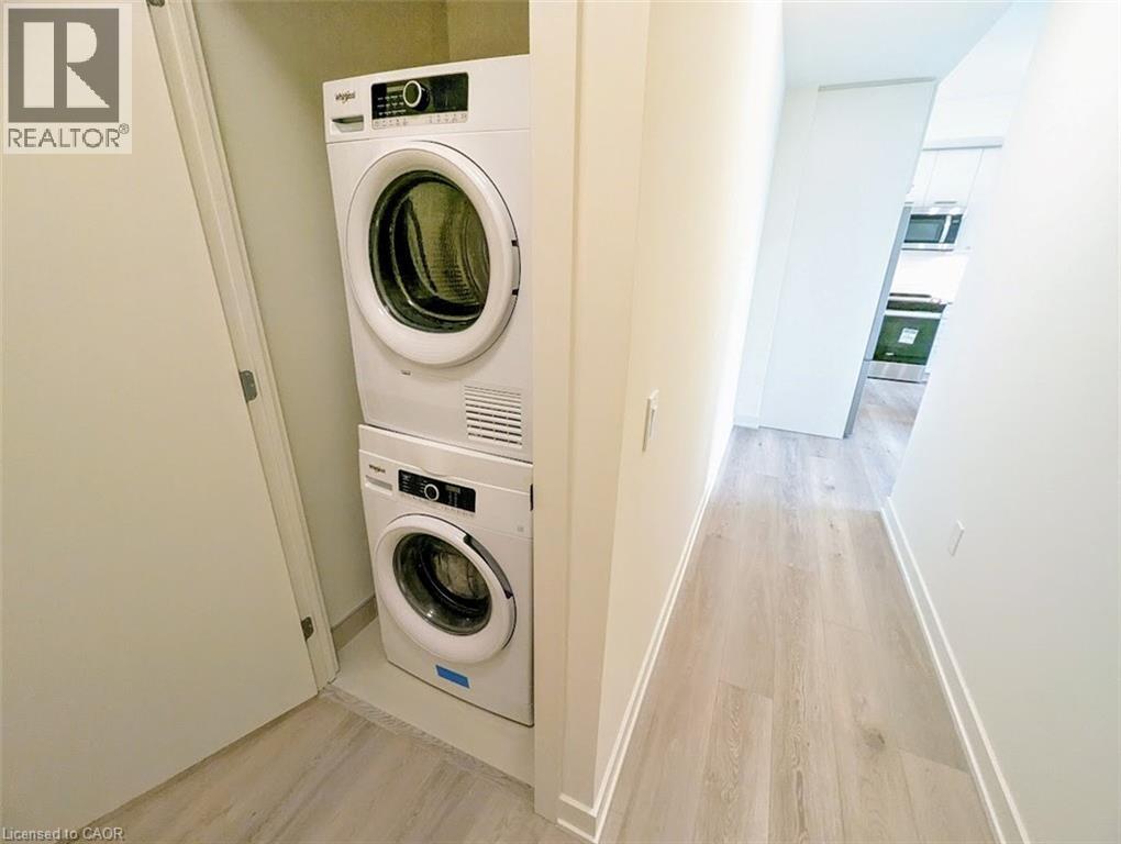 Laundry area with light wood-style floors and stacked washer and clothes dryer - 385 Winston Road Unit# 1311, Grimsby, ON - Indoor Photo Showing Laundry Room