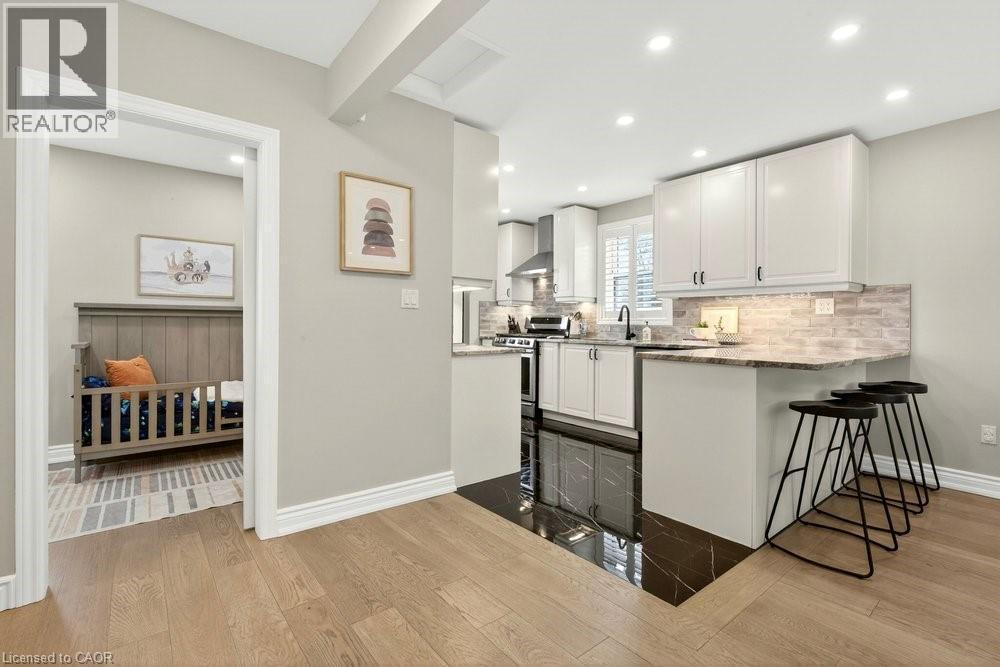 Kitchen with light stone countertops, a breakfast bar area, light wood-style floors, white cabinetry, and a peninsula - 237 East 32Nd Street, Hamilton, ON - Indoor Photo Showing Kitchen With Upgraded Kitchen