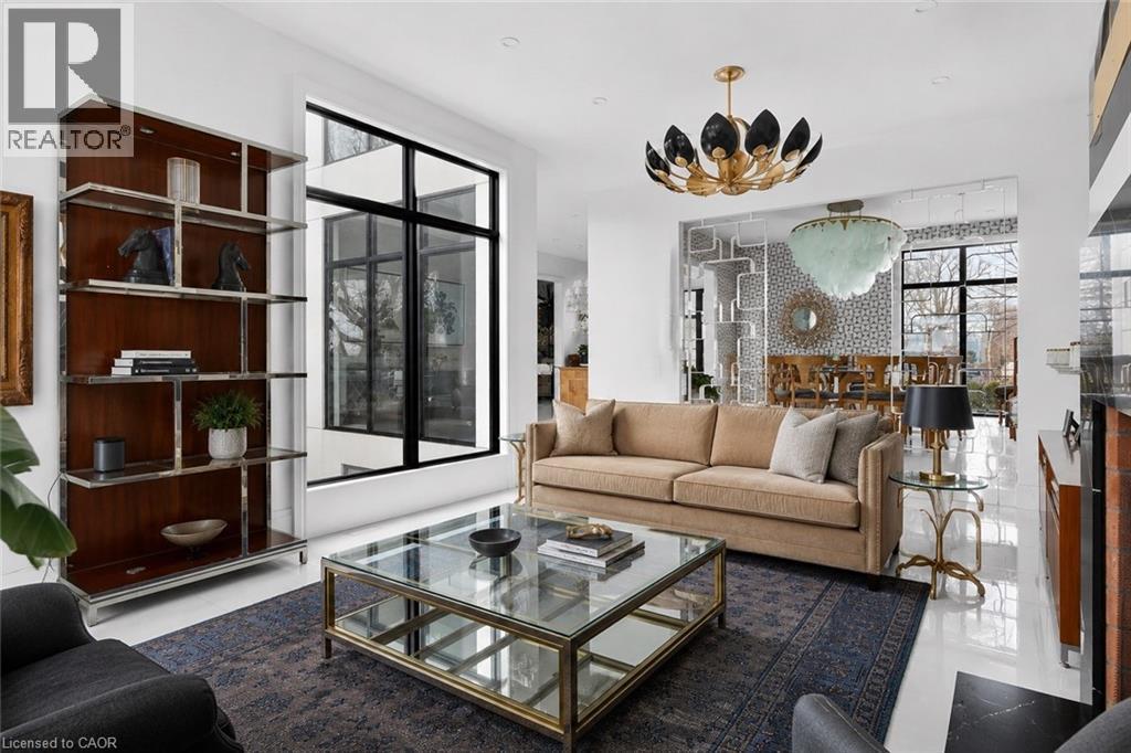 Spacious living area featuring polished white flooring, a built-in shelving unit with wood-finish backing and chrome accents, a full-height window with black frames, and a distinctive overhead light f - 711 Beach Boulevard, Hamilton, ON - Indoor Photo Showing Living Room