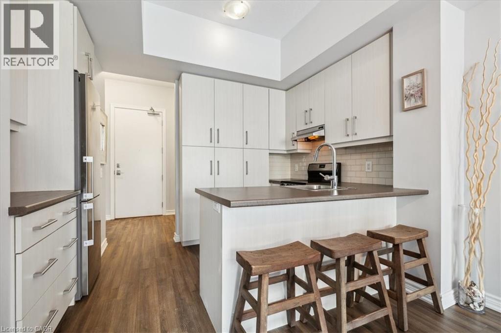 Kitchen with a breakfast bar area, a peninsula, dark countertops, and dark wood-style flooring - 40 Esplanade Lane Unit# 102, Grimsby, ON - Indoor Photo Showing Kitchen