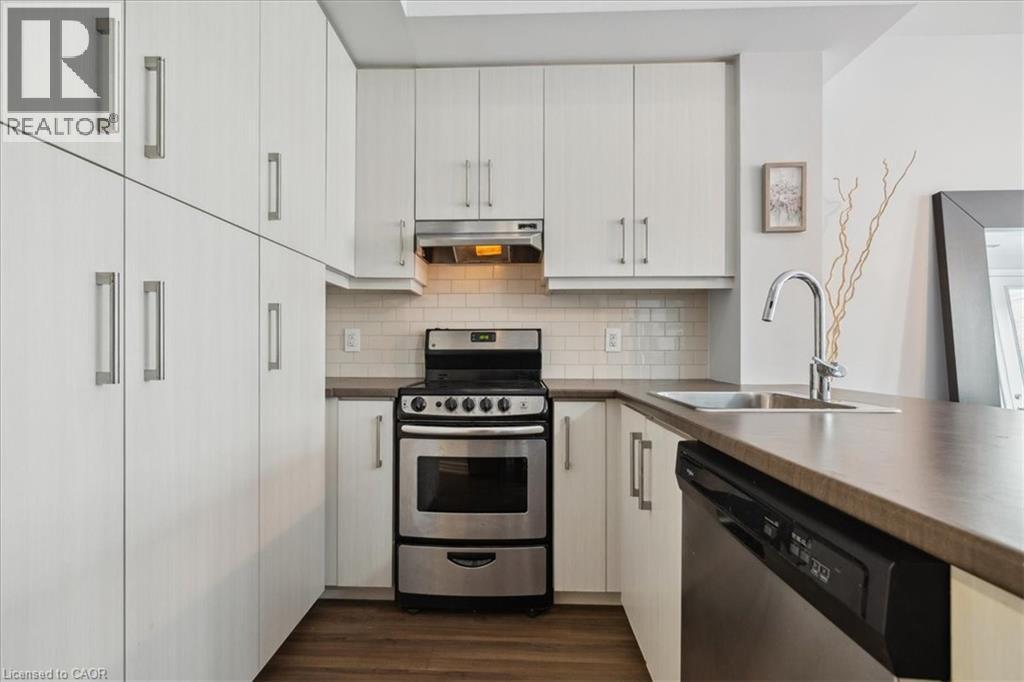 Kitchen with stainless steel appliances, dark wood-style flooring, tasteful backsplash, and white cabinetry - 40 Esplanade Lane Unit# 102, Grimsby, ON - Indoor Photo Showing Kitchen
