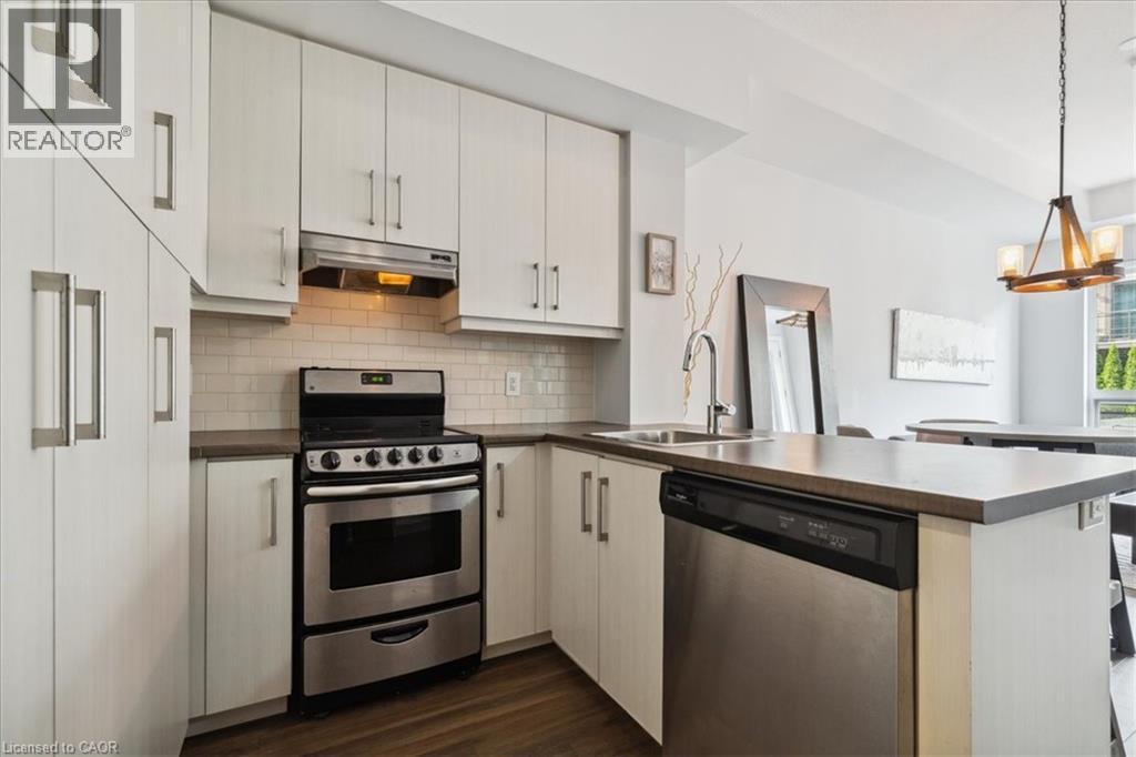 Kitchen with a peninsula, stainless steel appliances, dark wood-style flooring, backsplash, and dark countertops - 40 Esplanade Lane Unit# 102, Grimsby, ON - Indoor Photo Showing Kitchen