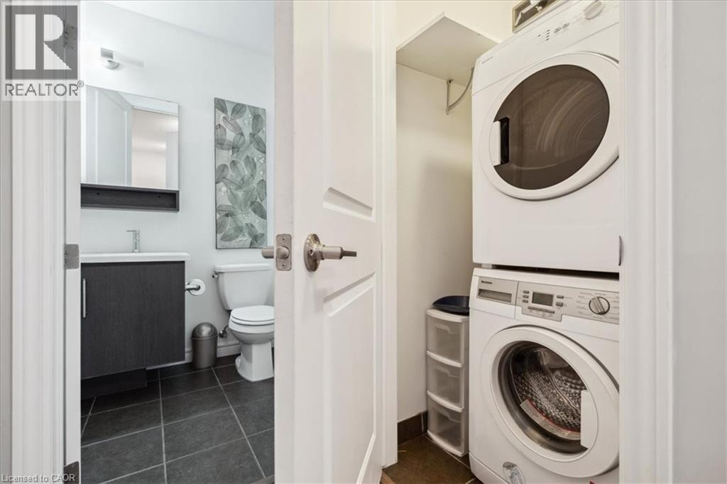 Laundry area featuring stacked washer and dryer and dark tile patterned flooring - 40 Esplanade Lane Unit# 102, Grimsby, ON - Indoor Photo Showing Laundry Room