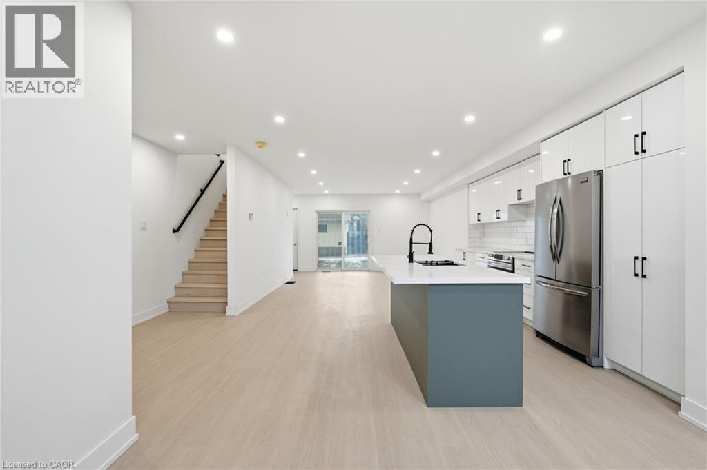 Kitchen with stainless steel appliances, an island with sink, light wood-type flooring, dual tone cabinetry, and backsplash - 1278 Main Street E, Hamilton, ON - Indoor Photo Showing Kitchen With Upgraded Kitchen