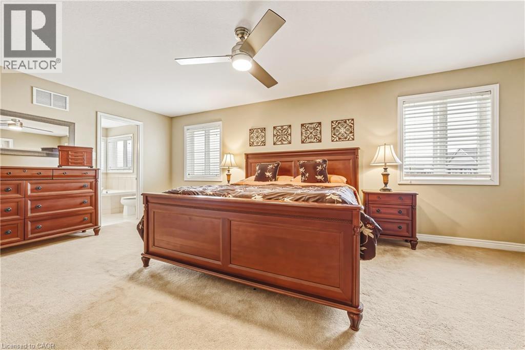 Bedroom featuring light carpet, multiple windows, a ceiling fan, and connected bathroom - 120 Valiant Circle, Hamilton, ON - Indoor Photo Showing Bedroom