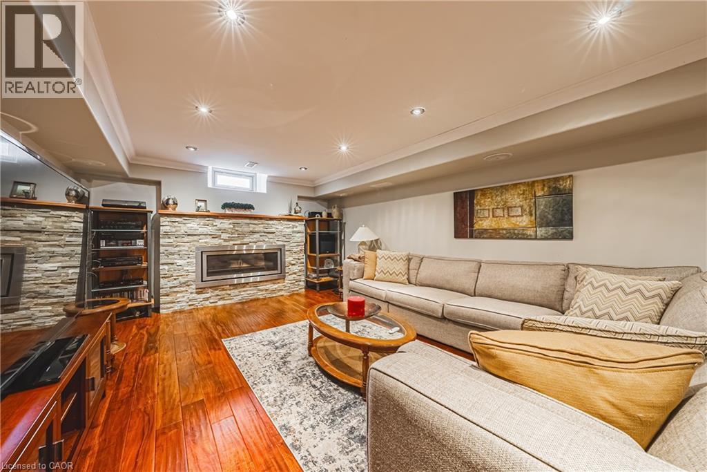 Living area featuring a stone fireplace, dark wood-type flooring, and crown molding - 120 Valiant Circle, Hamilton, ON - Indoor Photo Showing Living Room With Fireplace