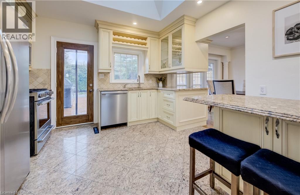 Kitchen with stainless steel appliances, light stone countertops, glass insert cabinets, granite tiled floors, and cream cabinetry - 655 Ellengale Road, Burlington, ON - Indoor Photo Showing Kitchen