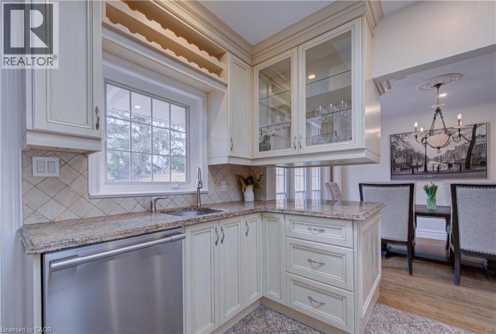 Kitchen with light stone counters, stainless steel dishwasher, glass fronted cabinets, hanging lights, and backsplash - 655 Ellengale Road, Burlington, ON - Indoor Photo Showing Kitchen