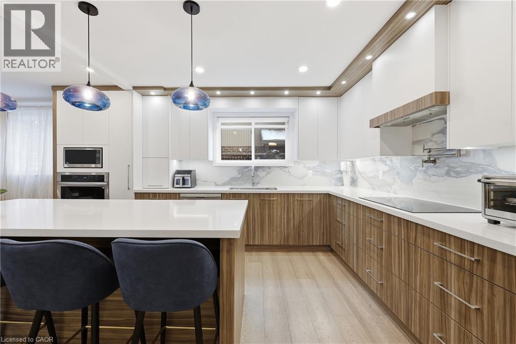 Two tone kitchen with two tone cabinetry, a kitchen breakfast bar, modern cabinets, stainless steel appliances, and light wood finished floors - 273 Bryant Crescent, Burlington, ON - Indoor Photo Showing Kitchen With Upgraded Kitchen