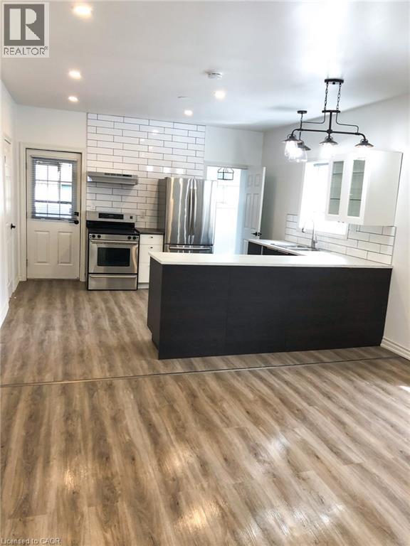 Dual tone kitchen featuring a peninsula, stainless steel appliances, healthy amount of natural light, tasteful backsplash, and dual tone cabinets - 57 New Street, Hamilton, ON - Indoor Photo Showing Kitchen With Fireplace