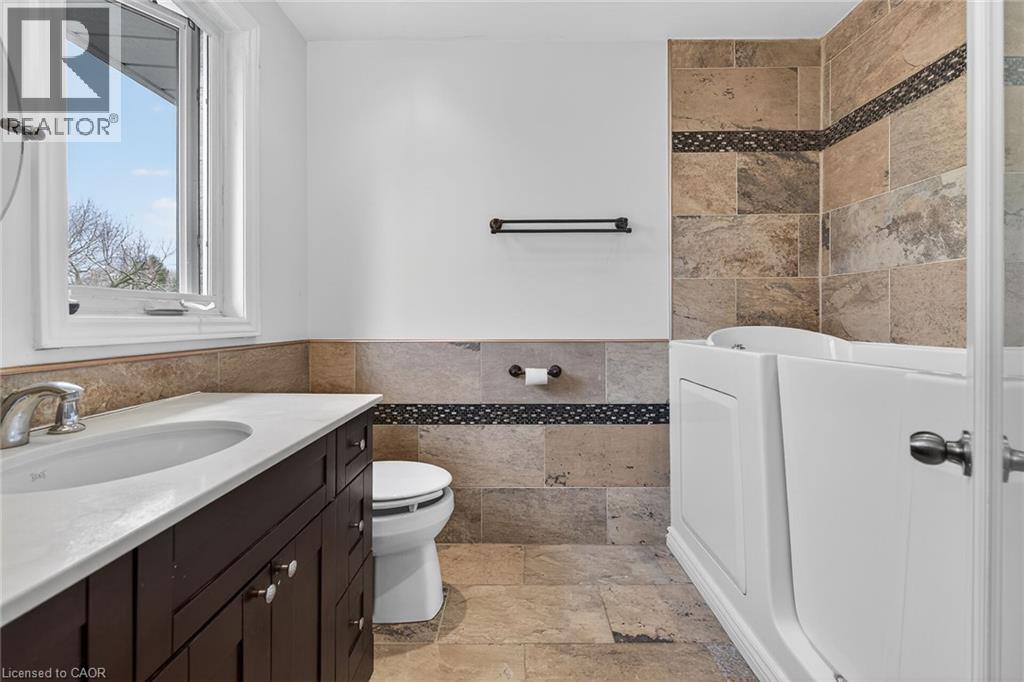Full bathroom with vanity, stone tile floors, tile walls, a bath, and wainscoting - 22 Woodside Drive, Hamilton, ON - Indoor Photo Showing Bathroom