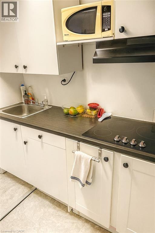 Kitchen with white cabinetry, ventilation hood, black electric cooktop, dark countertops, and light tile patterned floors - 988 Prosperity Court, London, ON - Indoor Photo Showing Kitchen With Double Sink