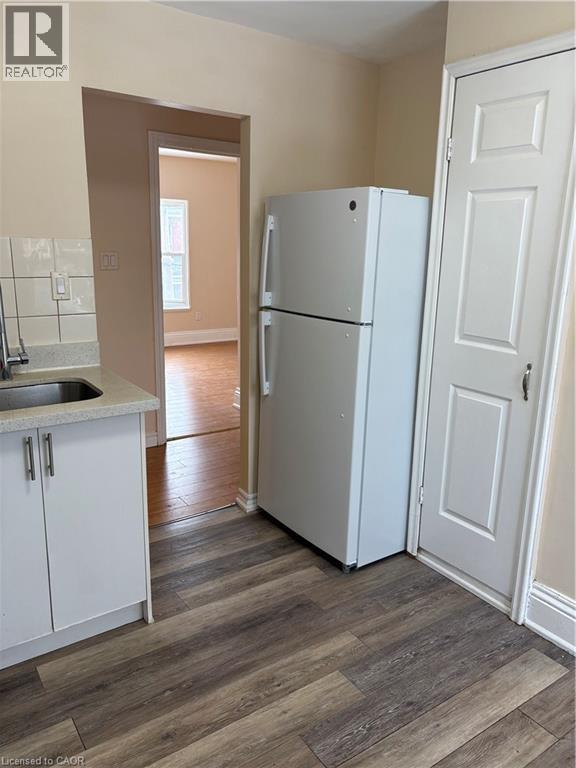 Kitchen with white refrigerator, dark wood finished floors, light stone countertops, white cabinetry, and tasteful backsplash - 95 Sanford Avenue N, Hamilton, ON - Indoor Photo Showing Kitchen