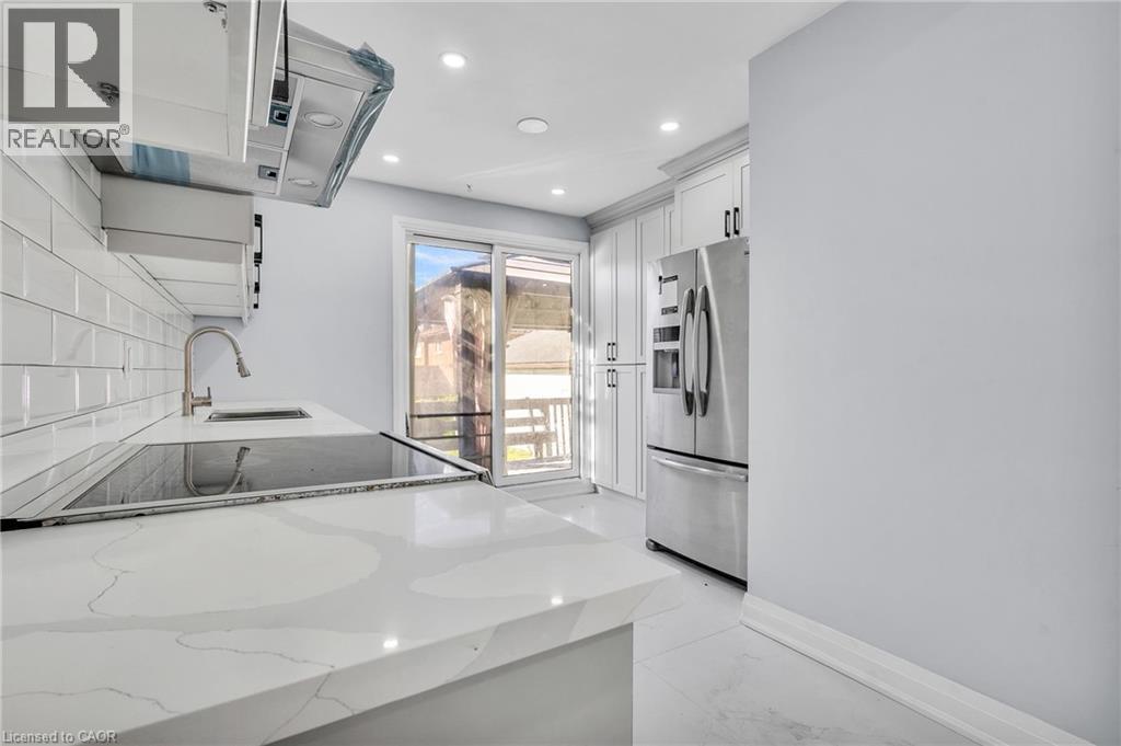 Kitchen featuring light stone countertops, ventilation hood, stainless steel fridge with ice dispenser, white cabinetry, and recessed lighting - 84 Avalon Place, Kitchener, ON - Indoor