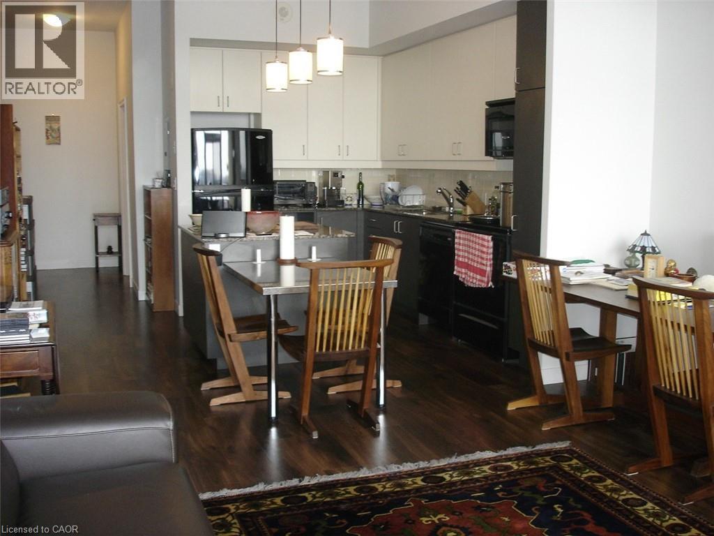 Dual tone kitchen featuring dark countertops, dark wood-style floors, black appliances, a kitchen bar, and a kitchen island - 191 King Street S Unit# 712, Waterloo, ON - Indoor